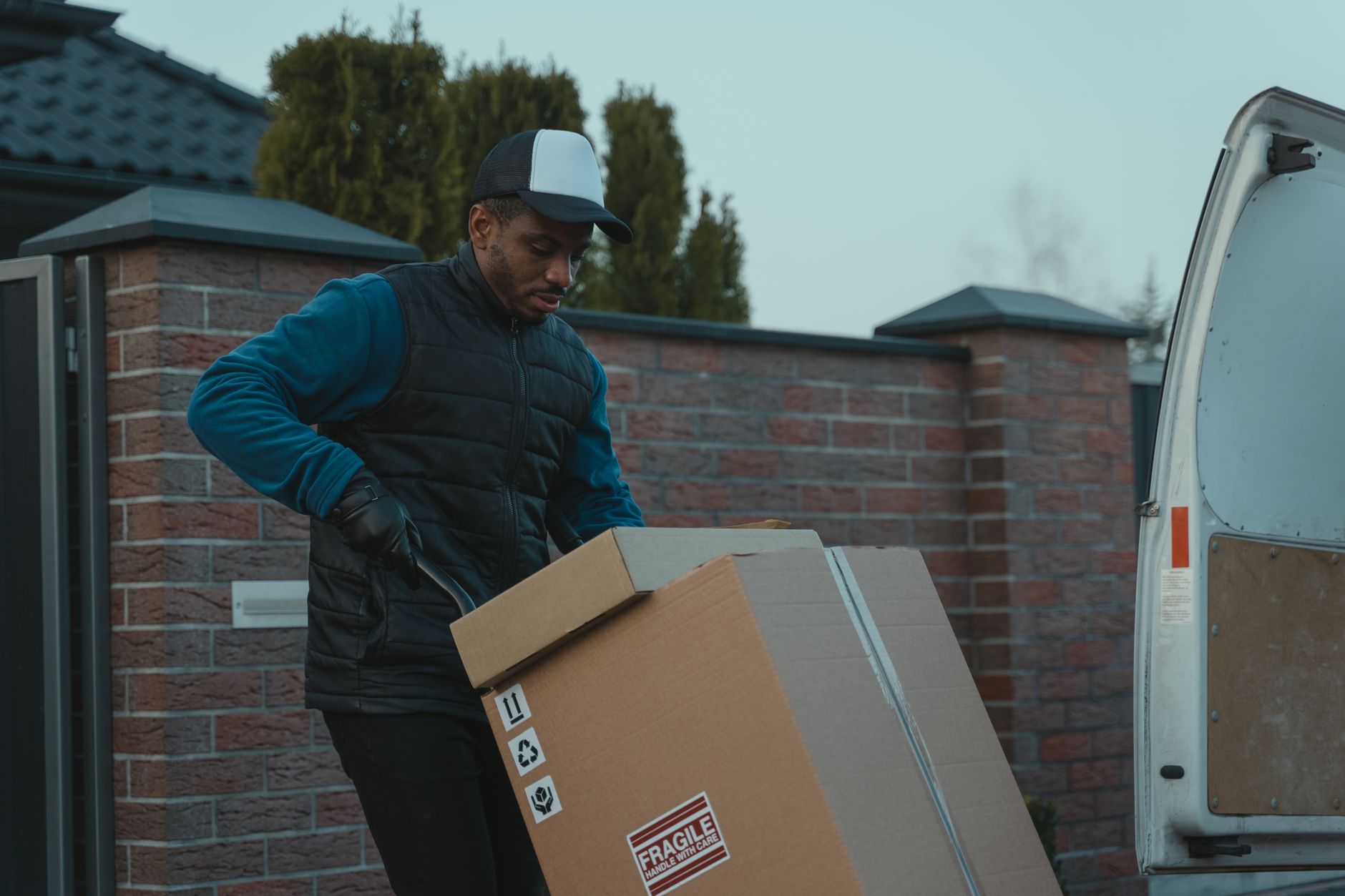 Two ordinary adult furniture delivery crew members carrying a wrapped armchair through the entrance of a UK terraced…
