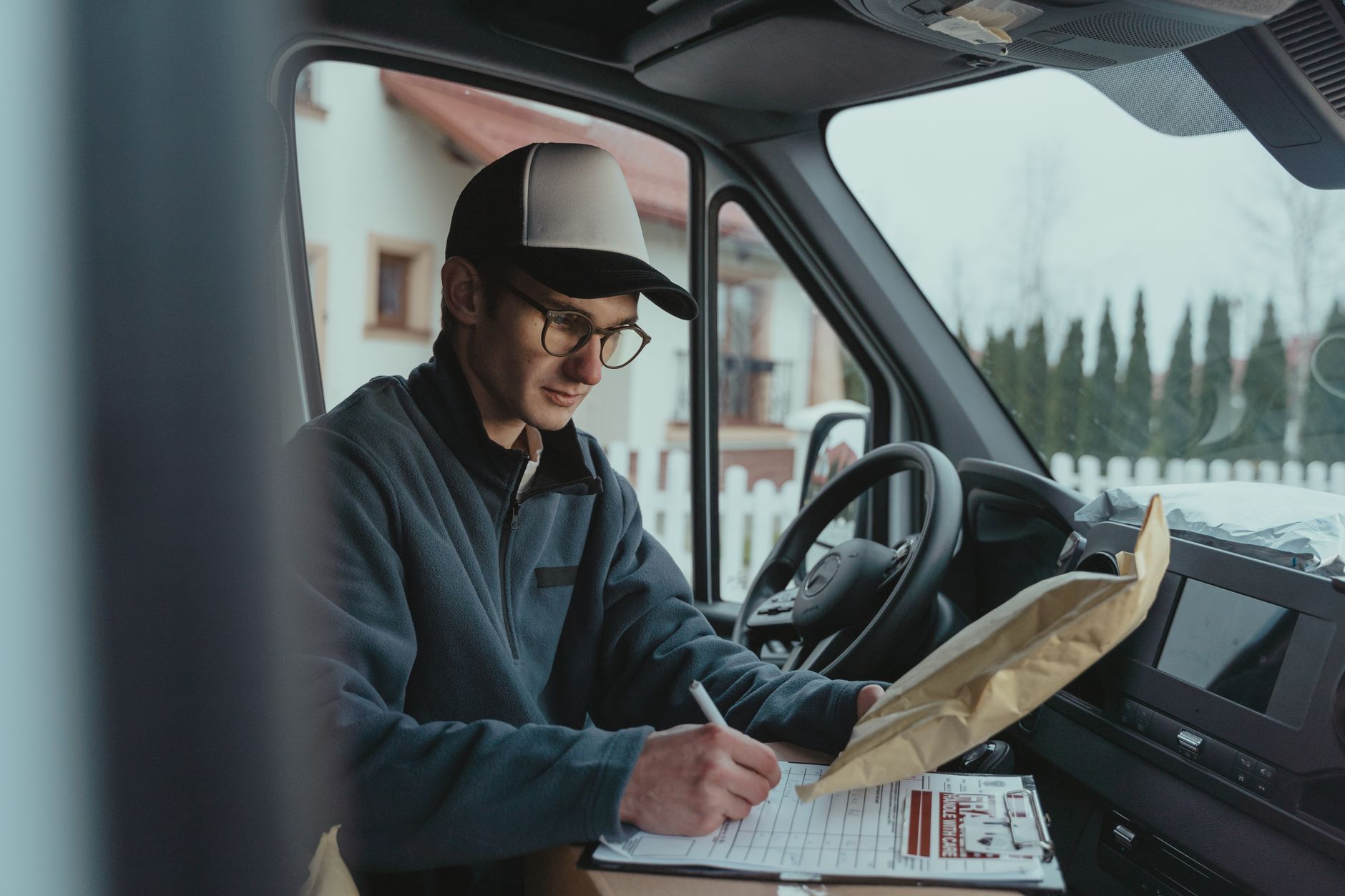 At a UK filling station: an ordinary delivery driver refuelling an unbranded panel van during the working day, natural…