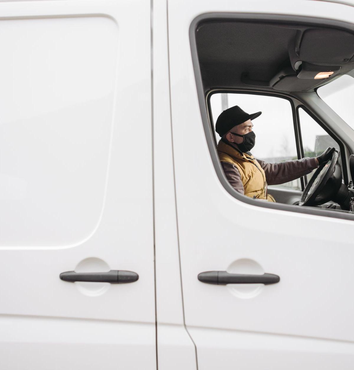At a UK contractor outbase on an overcast morning: an ordinary delivery driver in plain workwear adjusting a van wing…