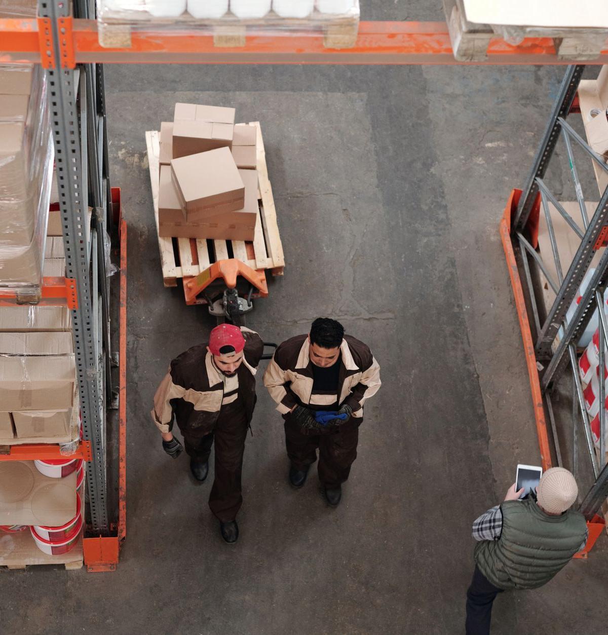 In a lived-in UK dining room: two ordinary delivery crew members gathering protective furniture wrapping beside a newly…