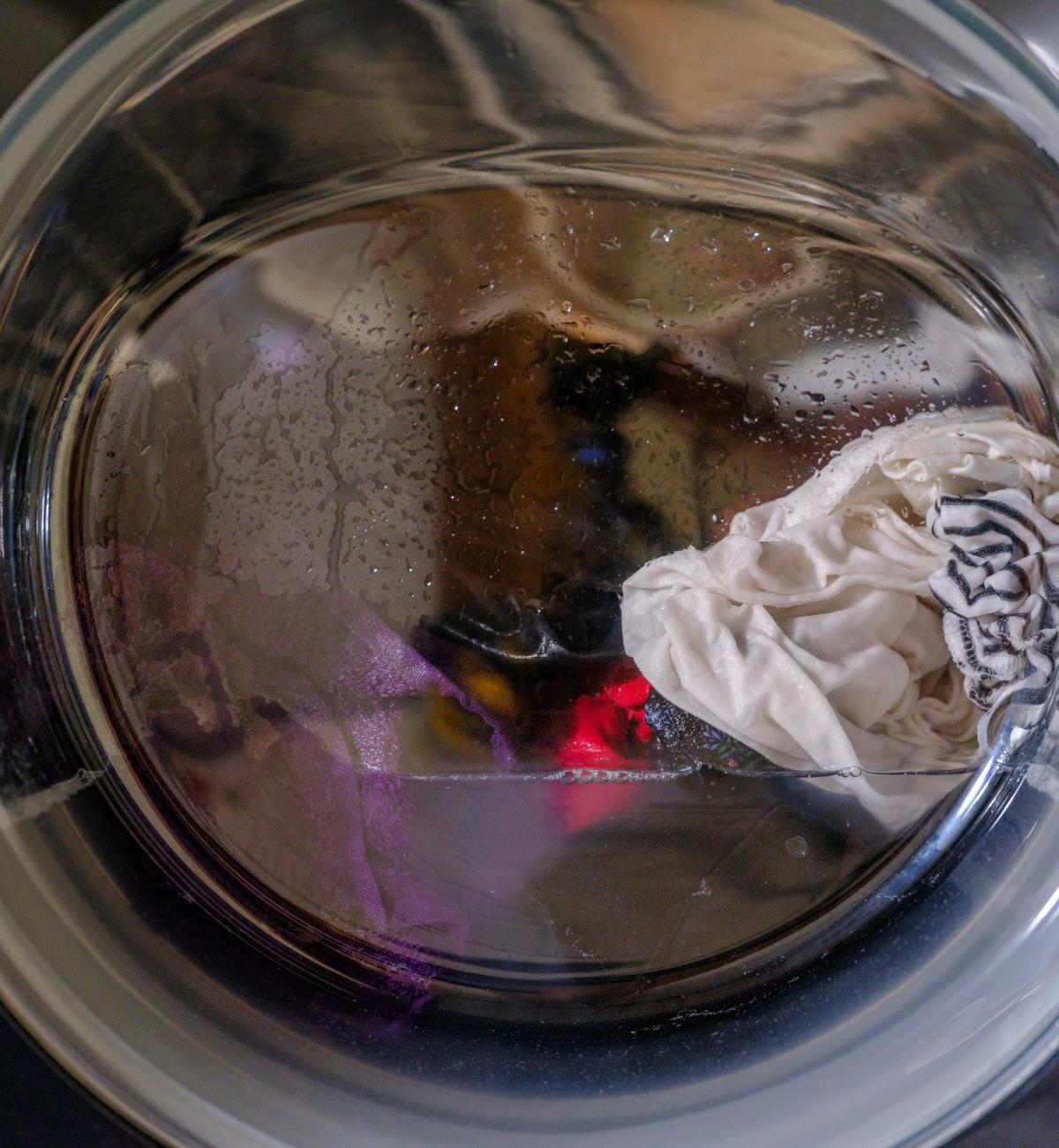 A self-employed appliance crew member checking the rear connections of a stationary washing machine in a modest UK…