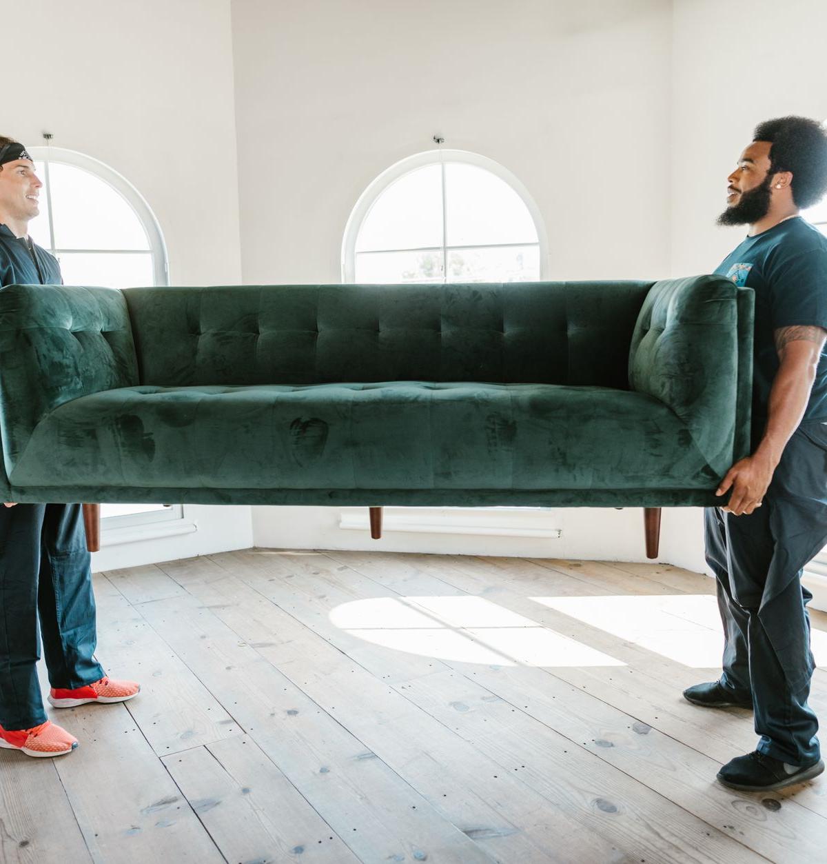 Two-person delivery crew carrying a large sofa into a living room