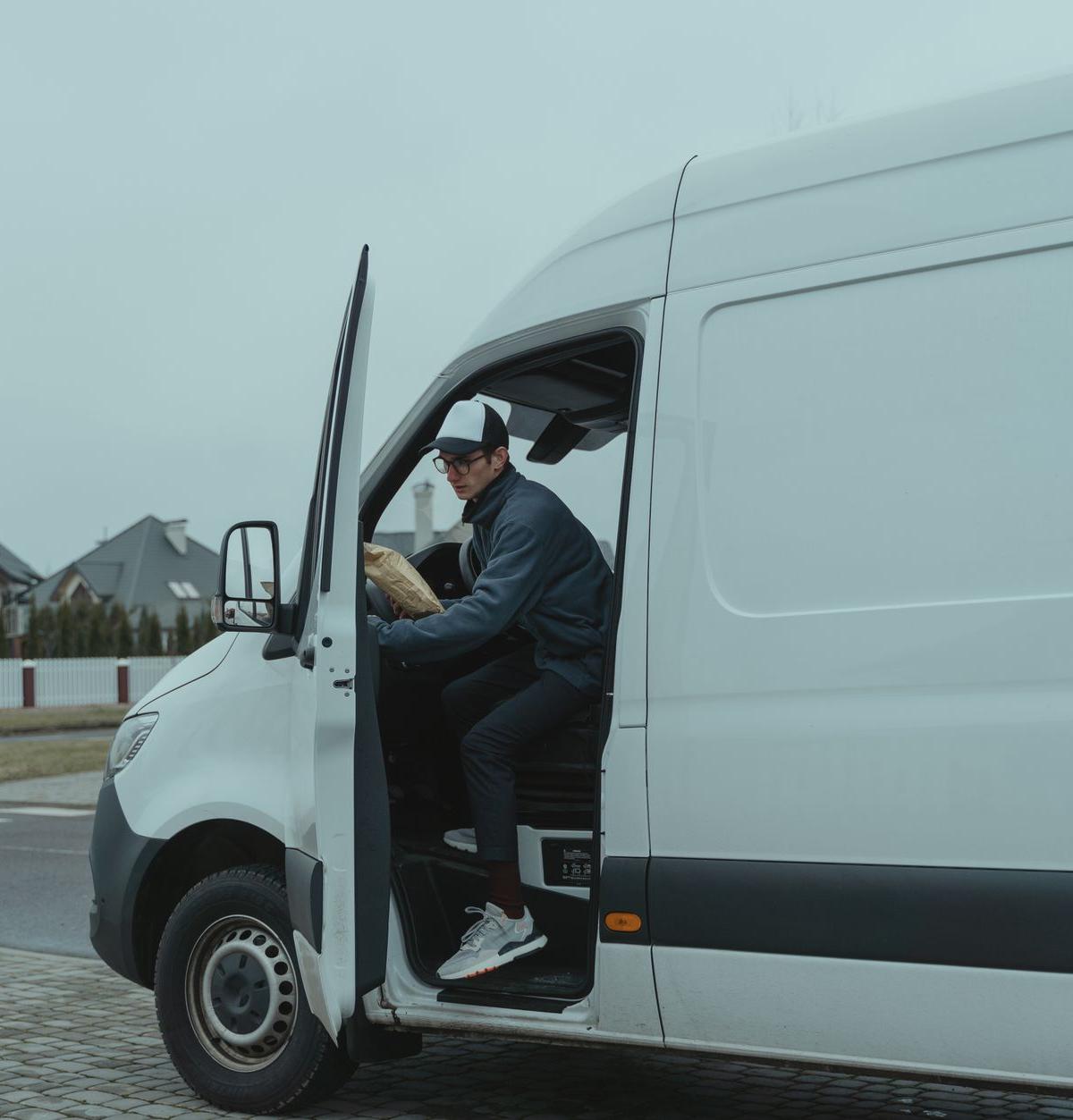 Side view of a delivery driver unloading a fridge from a van on a narrow residential street in the UK