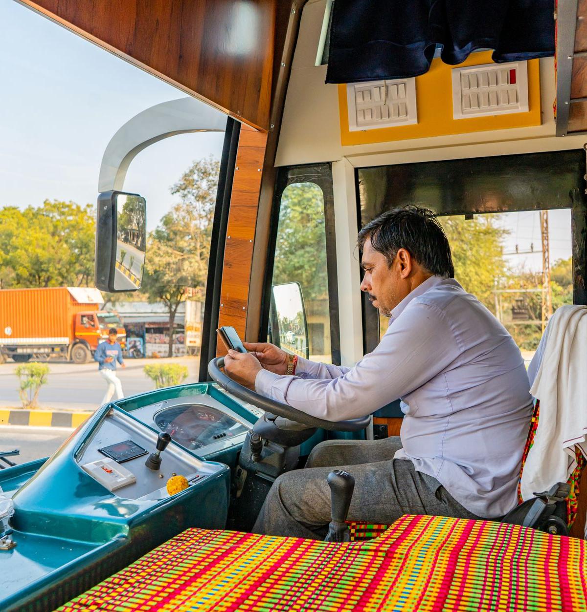 An ordinary experienced delivery driver sitting side-on in a parked van cab at a UK contractor outbase, checking a phone…